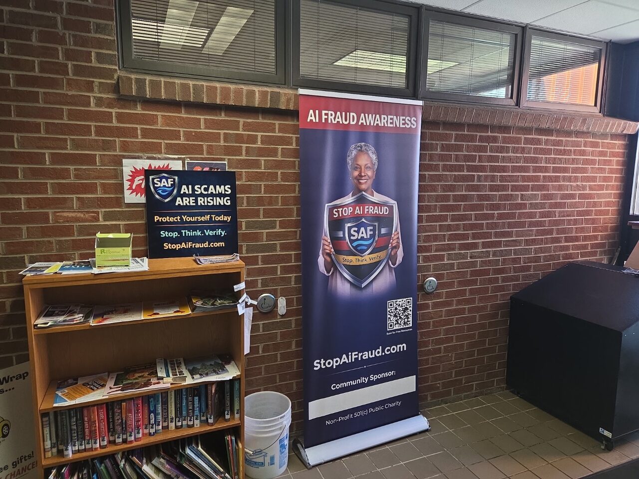 StopAiFraud community outreach setup featuring an "AI Scams Are Rising" banner and educational handouts in a public library.