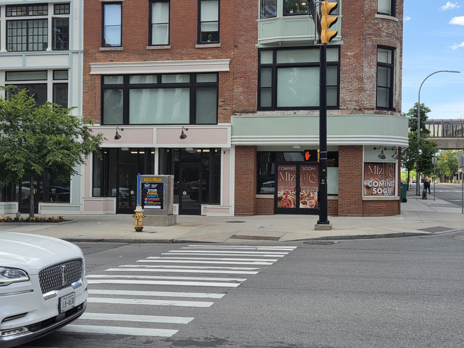 SAF Stop. Think. Verify. public safety sign installed on a traffic signal box at the Main & Clinton intersection in Downtown Rochester, NY β visible to drivers and pedestrians at a busy crosswalk.